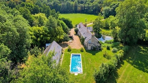 A large property with a swimming pool, multiple buildings, and a surrounding forest.