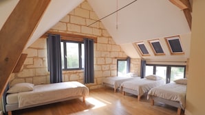 A bedroom with a sloped ceiling, wooden beams, and three beds.