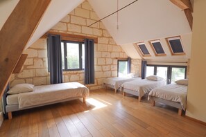 Ein Schlafzimmer mit schräg laufender Decke, Holzbalken und drei Betten.