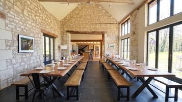 A long dining table with benches, set for a meal, in a room with stone walls and large windows.
