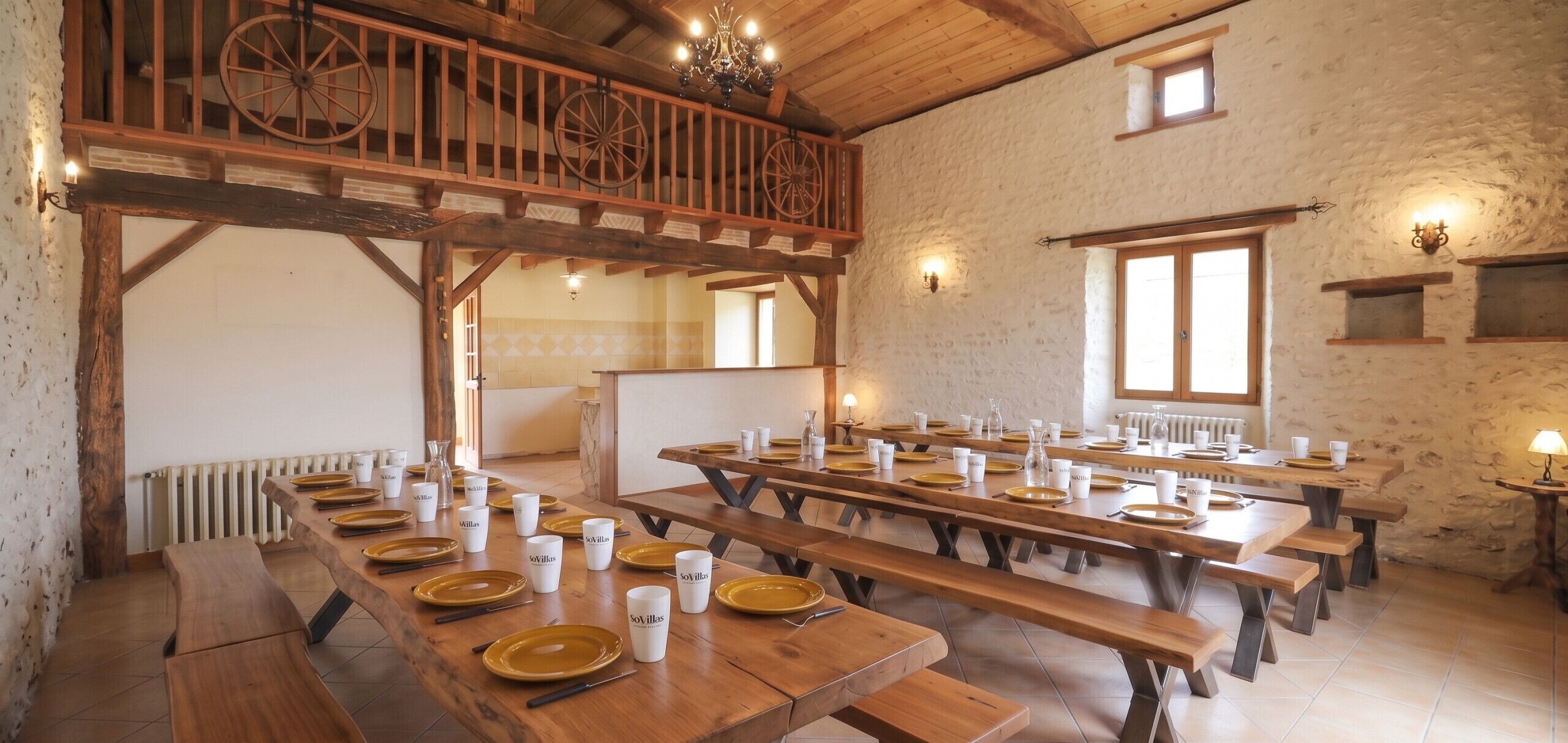 Un comedor rústico con mesas y bancos de madera, un balcón con barandilla de madera y una pared de piedra.