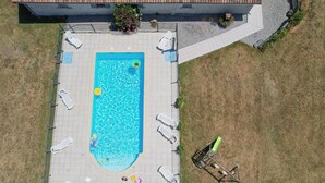 An aerial view of a rectangular swimming pool with multiple lounge chairs and a slide, surrounded by a paved deck and a grassy area. - So Villa Chez Penet (16) - Outdoor Pool - Beach Volleyball - 1 hour from Bordeaux - Sleeps 30. (Berneuil)