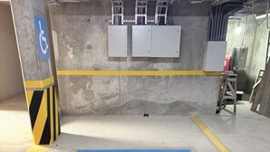 Pysäköintipaikka, joka on merkitty pyörätuolinkäyttöä symboloivalla merkillä, ja jonka ympärillä on keltaiset turvarajat ja jonka pohja on betonia.