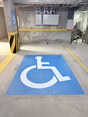 A parking space marked with a wheelchair accessibility symbol, surrounded by yellow safety lines and a concrete floor. - Coyote Tower 203 | Luxury Studio Walk to Marina (Cabo San Lucas)