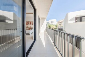 A modern balcony with a glass door leading to a bedroom, a clear view of the cityscape, and a white exterior wall. - Coyote Tower 203 | Luxury Studio Walk to Marina (Cabo San Lucas)
