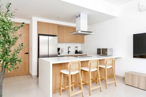 A modern kitchen with a central island, bar stools, a built-in oven, and a microwave. - Coyote Tower 203 | Luxury Studio Walk to Marina (Cabo San Lucas)