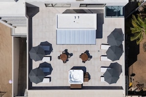 An aerial view of a rooftop terrace with a central seating area, surrounded by umbrellas, and a large rectangular structure. - Coyote Tower 203 | Luxury Studio Walk to Marina (Cabo San Lucas)
