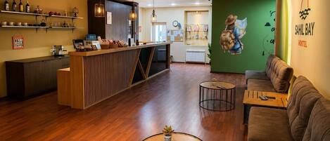 A reception area with a wooden counter, shelves with bottles, a green wall with a map mural, and a sofa.
