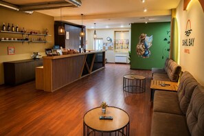A reception area with a wooden counter, shelves with bottles, a green wall with a map mural, and a sofa.