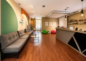 A modern hostel interior with a sofa, round tables, a reception desk, and artwork on the walls.