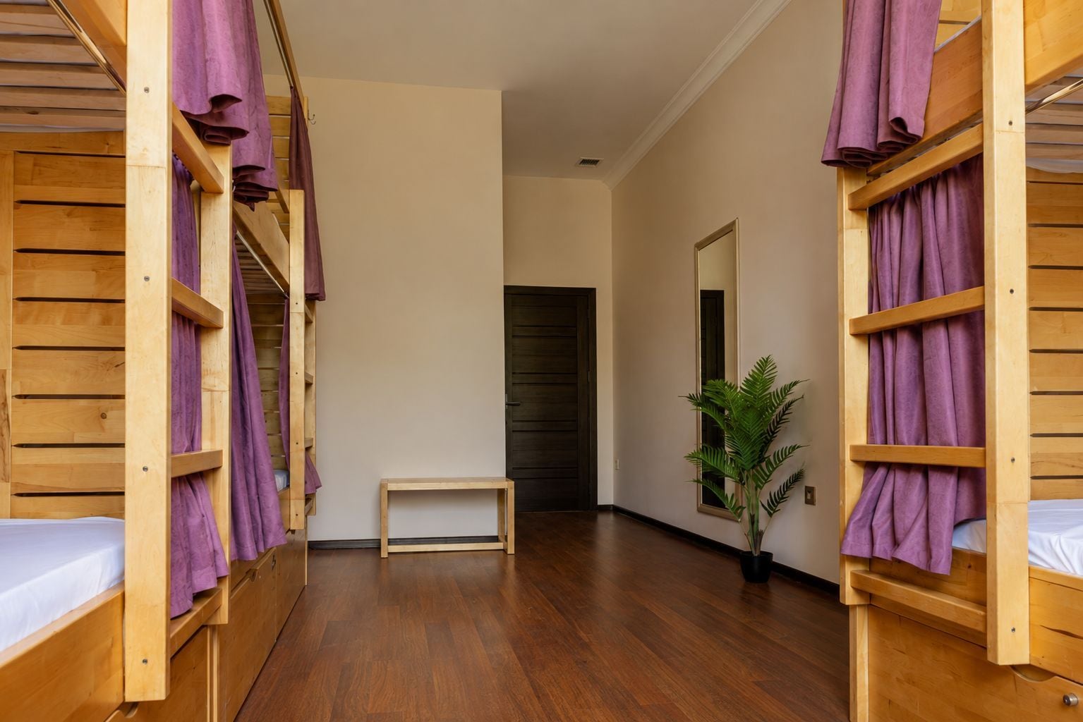 Quarto com beliches de madeira, uma mesinha e um vaso de planta.