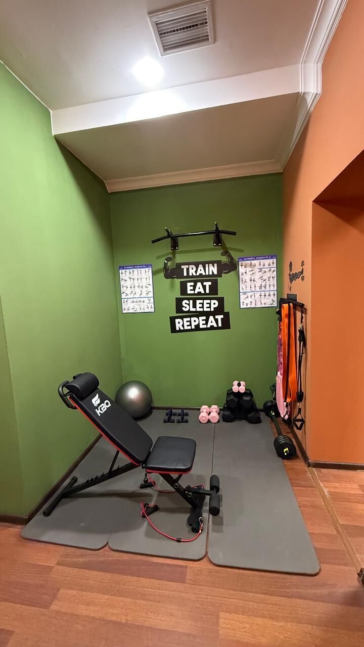 Uma academia em casa com equipamentos de ginástica, barra de pull-up e pôsteres motivacionais na parede.