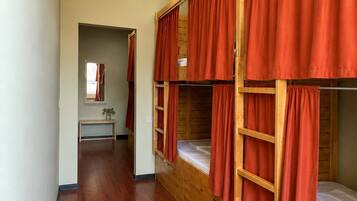 A room with bunk beds, wooden flooring, a mirror, and a small table.