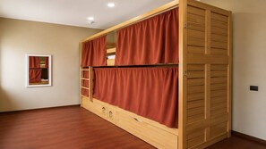 A room with a bunk bed, wooden flooring, and a mirror on the wall.