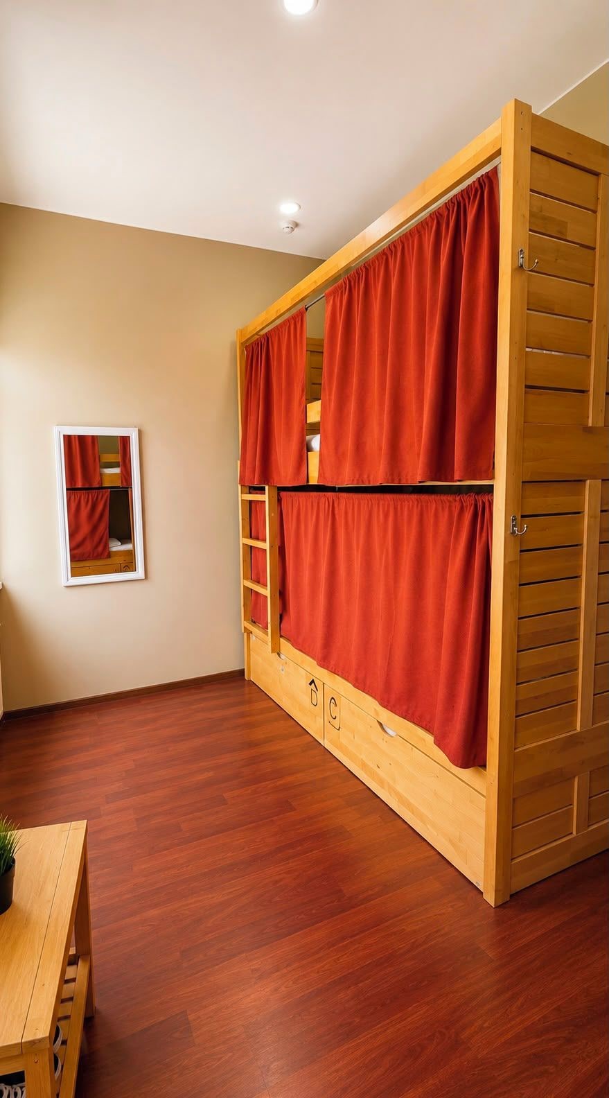 Uma cama de solteiro com cortinas vermelhas, uma escrivaninha de madeira e um quadro na parede.