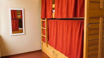 Uma cama de solteiro com cortinas vermelhas, uma escrivaninha de madeira e um quadro na parede.