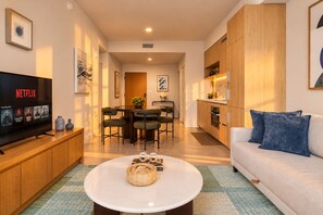 A modern living room with a flat-screen TV, a dining area with a table and chairs, a kitchen with wooden cabinets, and a sofa with blue cushions. - Miami Urban Retreat (Miami)