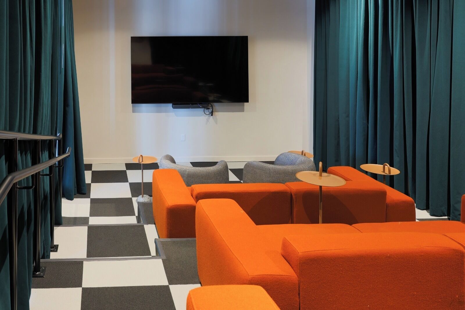 A modern living room with orange sofas, a flat-screen TV, and checkered flooring.