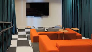 A modern living room with orange sofas, a flat-screen TV, and checkered flooring.
