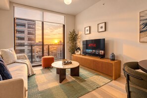 Una sala de estar moderna con un ventanal grande, un televisor de pantalla plana, un sofá, una mesa de centro y una mesita auxiliar.