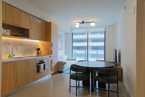 Una cocina moderna con armarios de madera, horno empotrado y comedor con una mesa redonda y cuatro sillas.