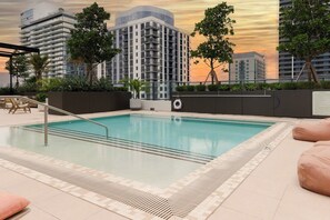 Una piscina con una escalera metálica, rodeada por un bordeado de baldosas y un muro bajo con plantas.