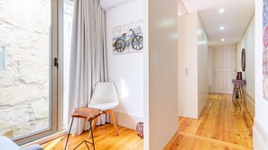Una habitación con pared de piedra, una silla blanca, un taburete de madera, una obra de arte de bicicleta y suelo de madera.