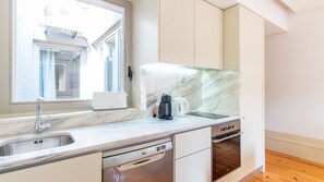 A modern kitchen with a built-in dishwasher, a coffee maker, and a kettle on the countertop. - Cedofeita Boutique Flat w/ AC by LovelyStay (Porto)