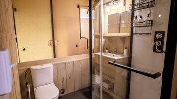 A compact bathroom with a toilet, a glass shower enclosure, and a sink with a soap dispenser.