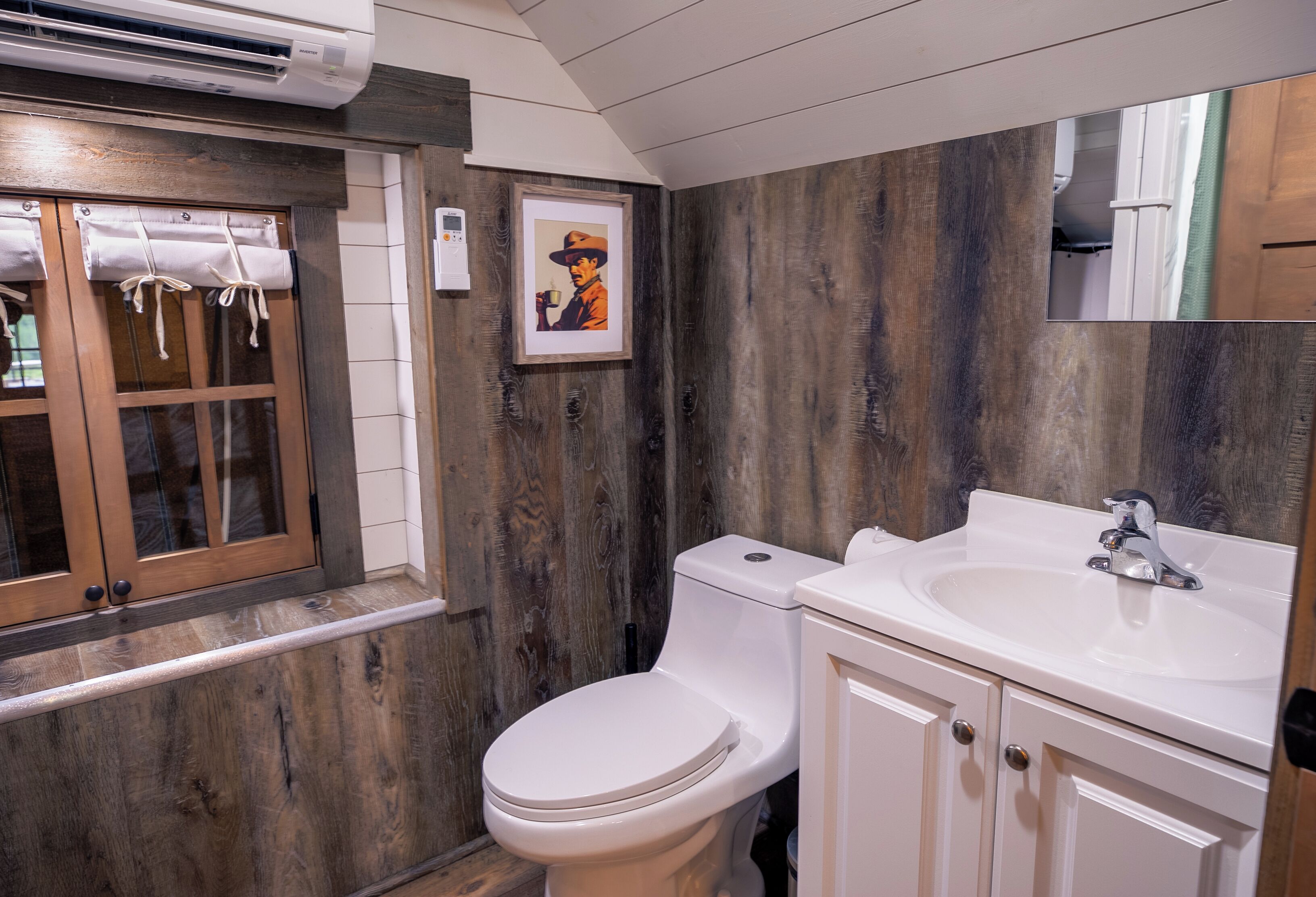 A bathroom with a wooden wall, a white toilet, a sink, and a window with curtains.