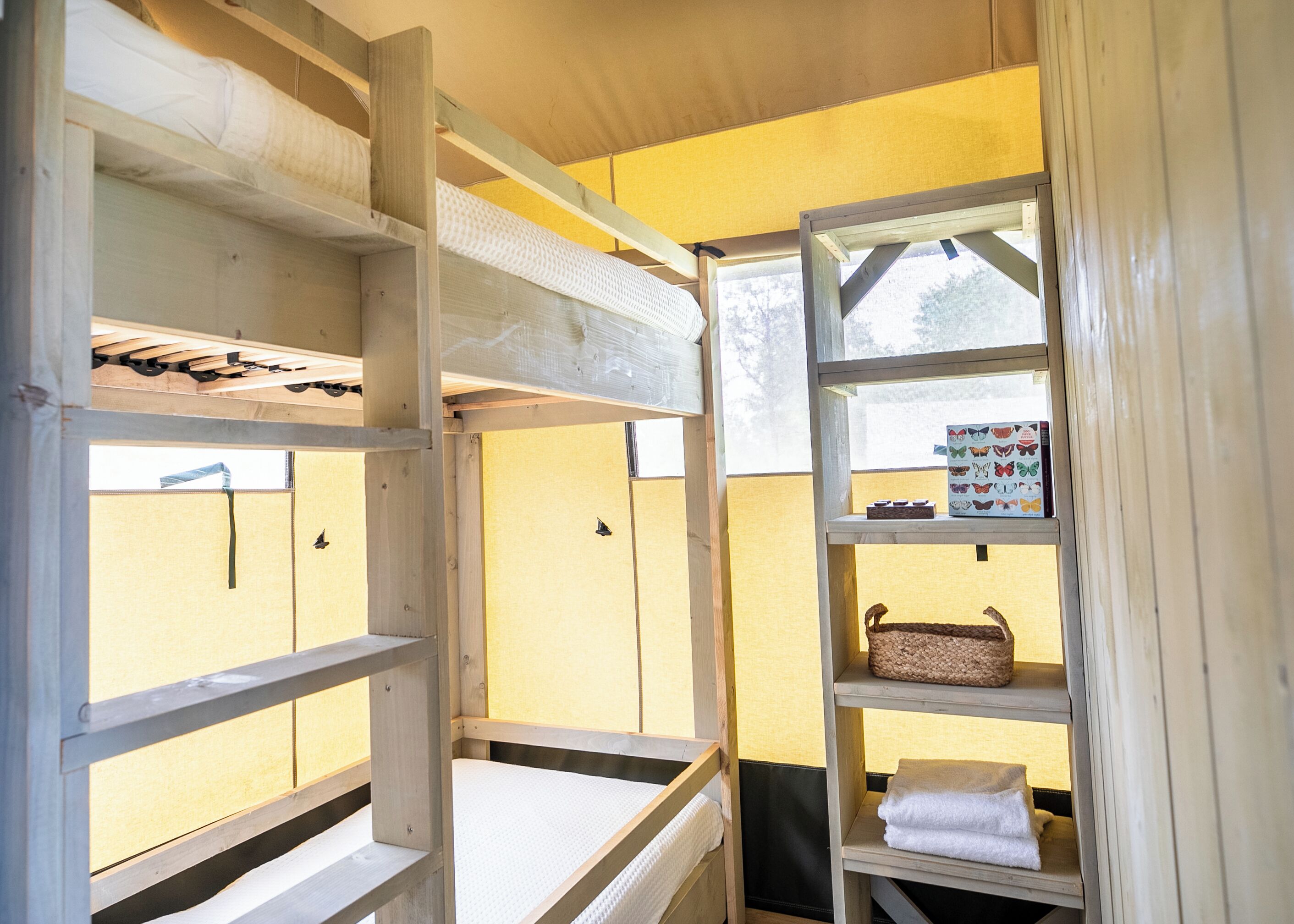 A bunk bed with a shelf unit beside it, containing a basket and a box of butterfly stickers.