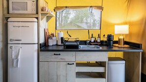 Una kitchenette compacta con microondas, refrigerador, lavamanos y ventana con vista a árboles.