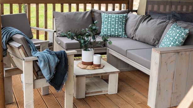 Una terraza de madera con un sofá, dos sillones, una mesita y una planta en maceta.