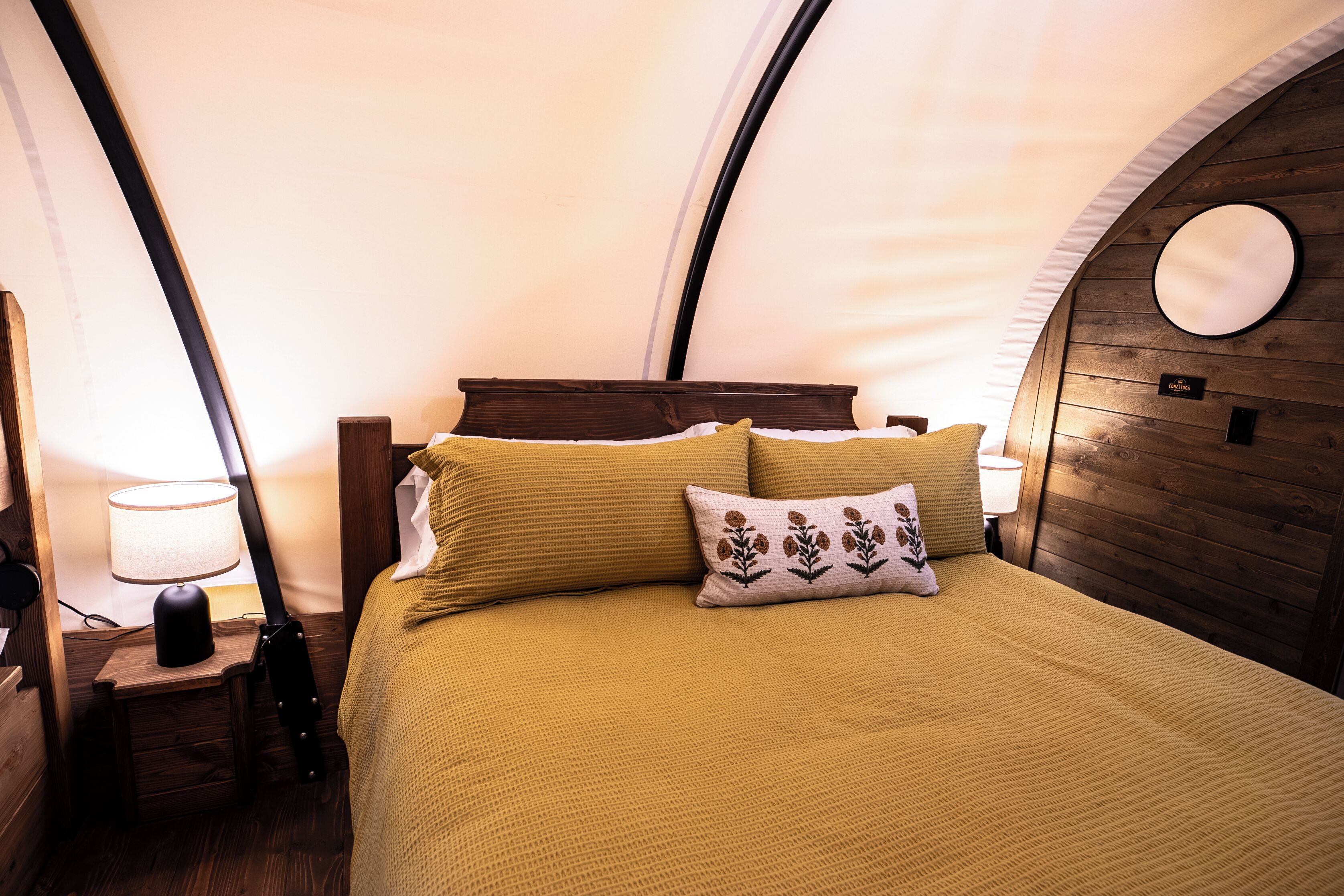 A cozy room with a bed, a lamp, and a circular mirror on the wall.