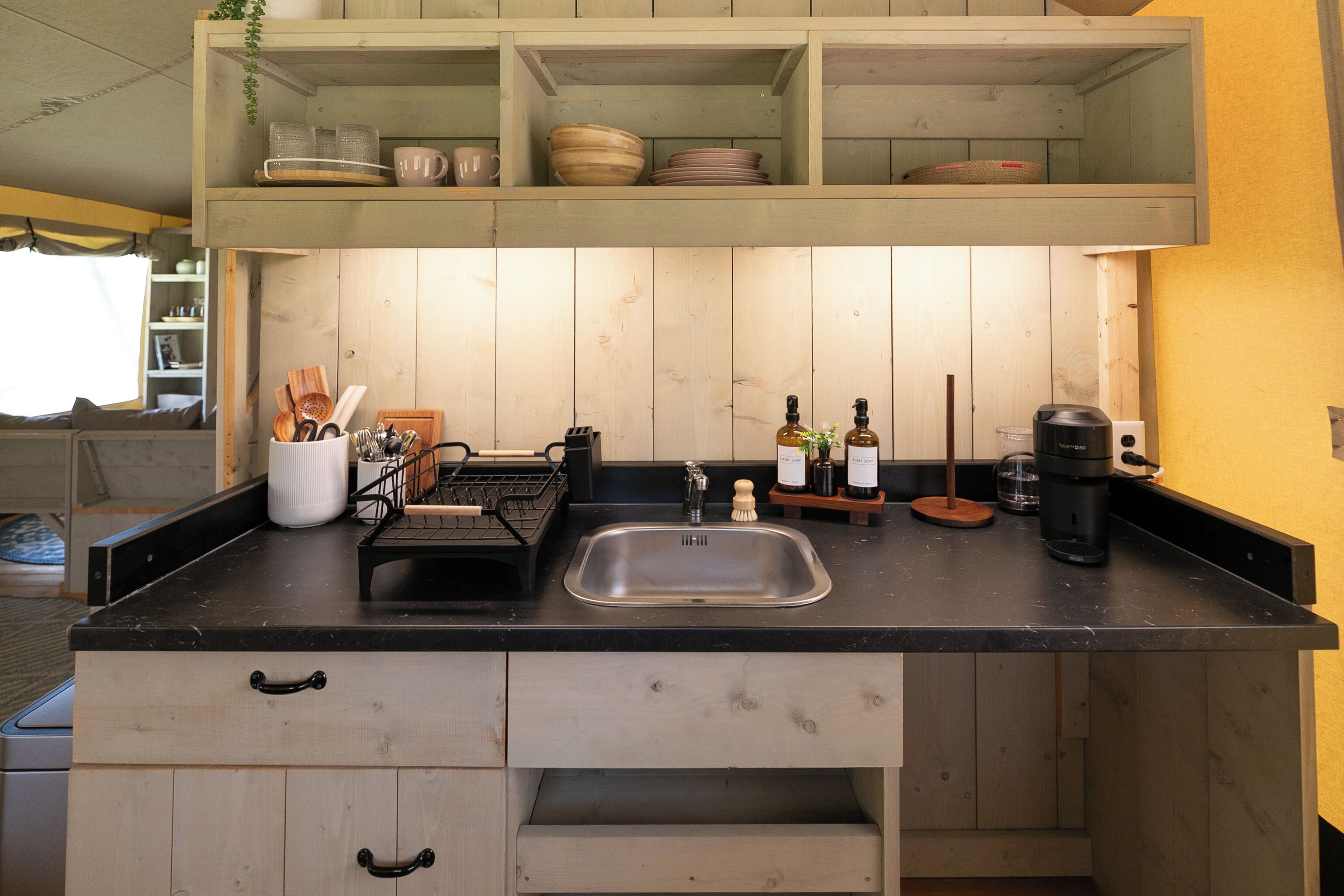 Une cuisine de taille réduite, dotée de meubles en bois, d’un plan de travail noir, d’un évier et de divers ustensiles de cuisine.