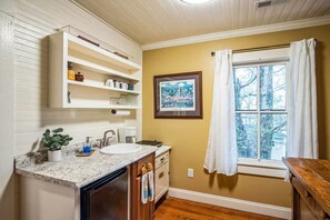 A bathroom with a sink, countertop, cabinets, and a window with curtains.
