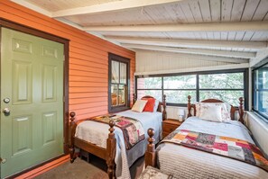 A bedroom with two beds, a green door, and a window with a view of trees.