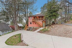 Ein zweigeschossiges Haus mit Balkon, Auffahrt und kleiner Gartenhütte.