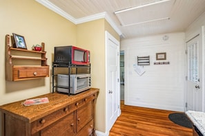 A room with a wooden cabinet, a microwave, and a toaster oven. There is a door leading to another room.