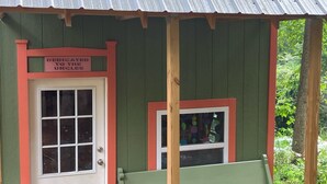 A small, rustic building with a green exterior and a red door. There is a bench outside and a window with a view of the surrounding greenery. - Vintage Saluda Escape Near Waterfalls (Saluda)