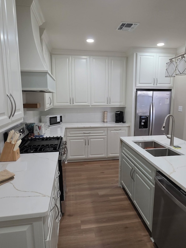 A modern kitchen with white cabinets, stainless steel appliances, and a wooden floor.