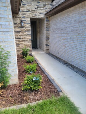 A stone exterior with a door and a small garden area with mulch and plants.