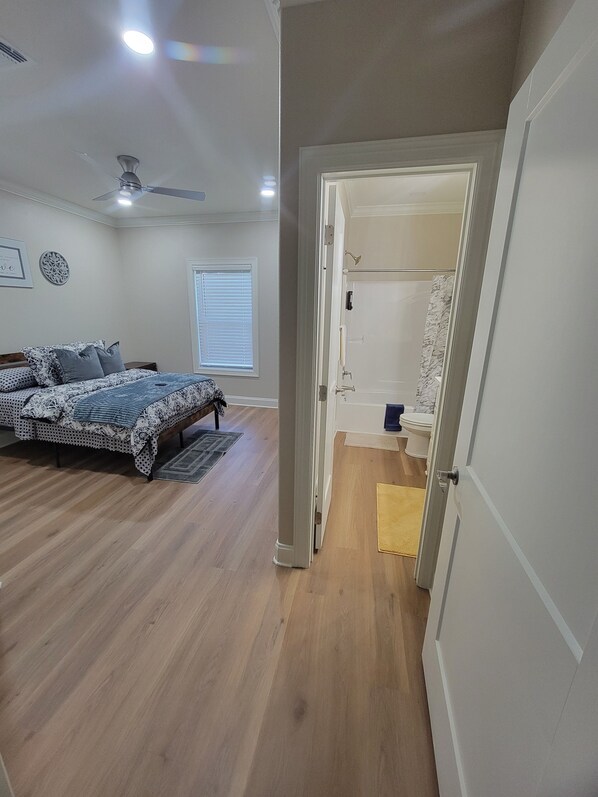 A bedroom with a bed, a ceiling fan, and a bathroom with a shower and toilet.