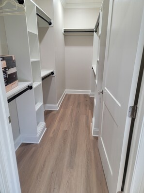 A walk-in closet with white shelving units, a wooden floor, and a door on the right.