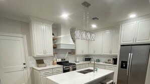 Een moderne keuken met witte kasten, een centraal eiland met barkrukken, roestvrijstalen apparatuur en een hanglamp.