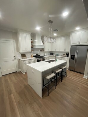 A modern kitchen with white cabinetry, a central island with bar stools, stainless steel appliances, and a pendant light fixture.