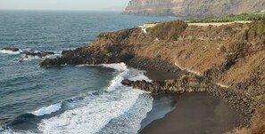 A coastal landscape with rocky cliffs, a beach, and a path leading up to a cliff-top viewpoint. - Excellent apartment with splendid ocean views (Puerto de la Cruz)
