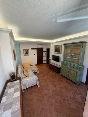 Ein Zimmer mit einem Bett, einem Fernseher, einem Schrank und einem gefliesten Boden.