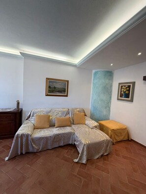 Ein Zimmer mit Schlafsessel, kleinem Tisch und zwei gerahmten Bildern an der Wand.