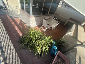 Eine Terrasse mit Tisch und Stühlen, einem Blumentopf und einer blauen Wasserkanne.